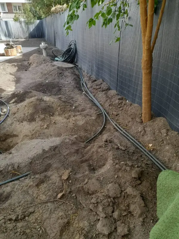Zanja con tuberías de riego junto a la valla durante la obra