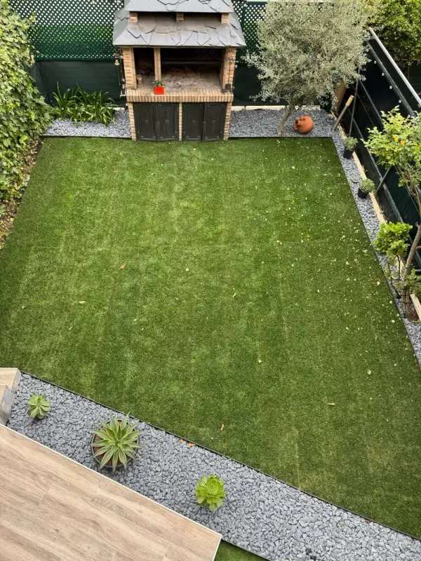 Jardín alargado con césped, grava decorativa y barbacoa al fondo