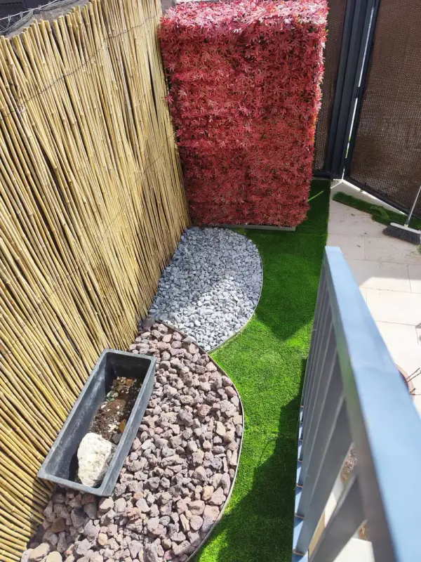Terraza estrecha con cañizo, parterres de piedra decorativa y césped artificial